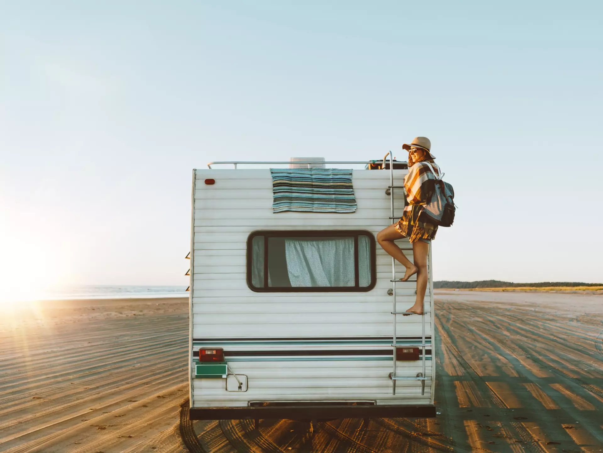 Young woman on the back of an RV, which is parked on the beach during sunset