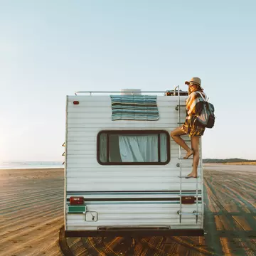 Young woman on the back of an RV, which is parked on the beach during sunset