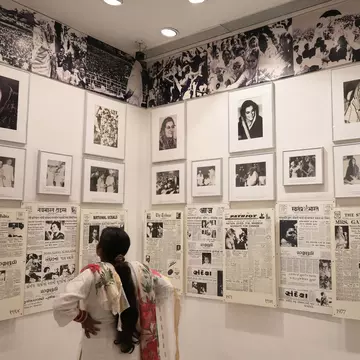Woman viewing a wall display of framed historical photographs and newspaper clippings related to Indira Gandhi's political career. New Delhi, India.
