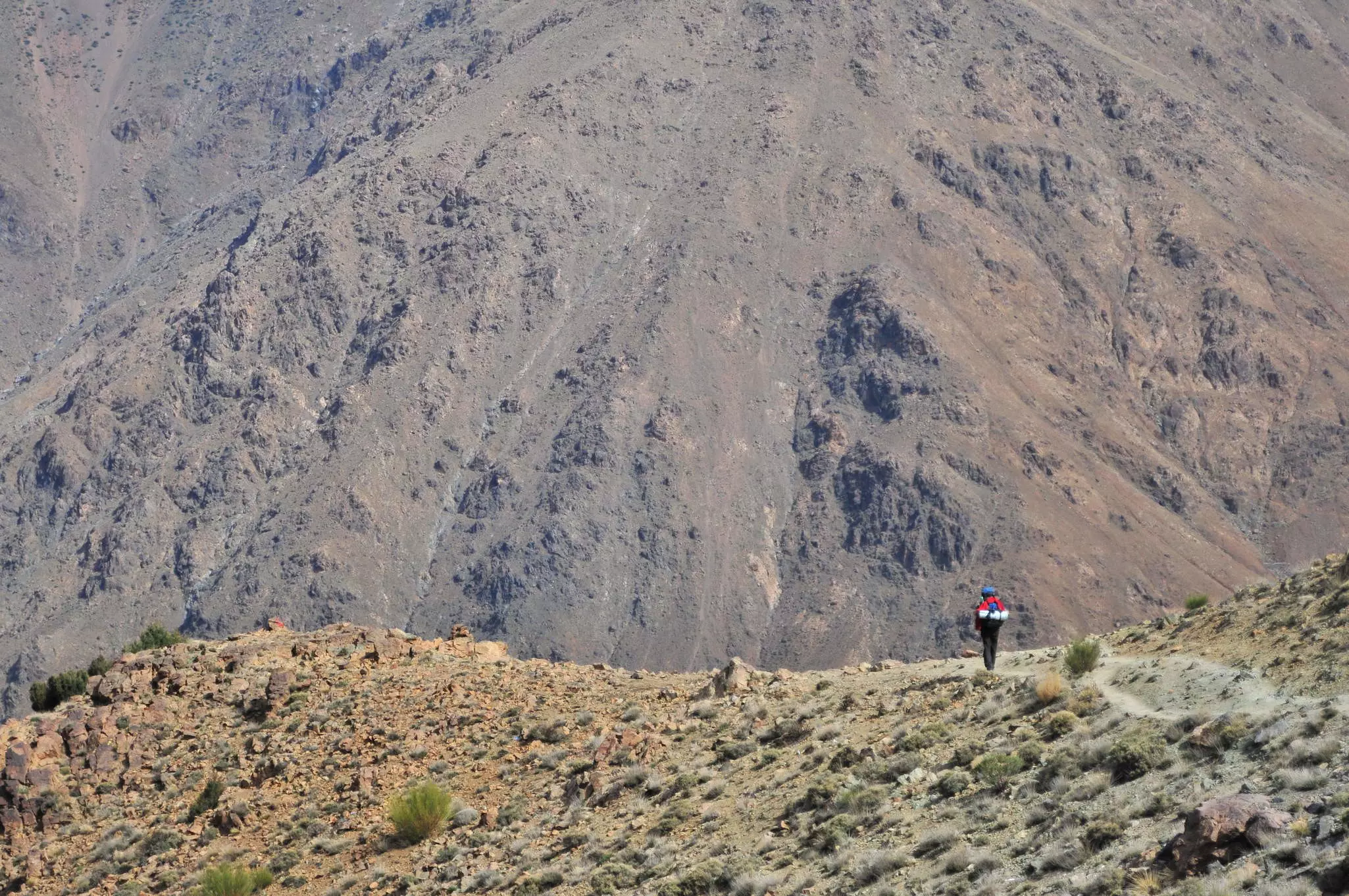 A lone hiker on a ridge who is dwarfed by the hulking mass of Jebel Toubkal in the background.