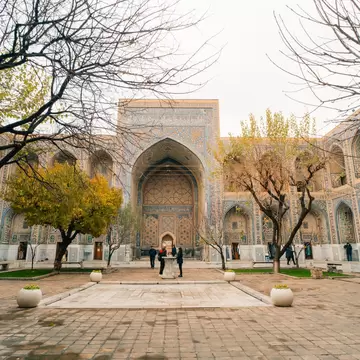 Tiled courtyard of a madrasah on Registan Square, Samarkand, Uzbekistan, with autumn trees and a few visitors