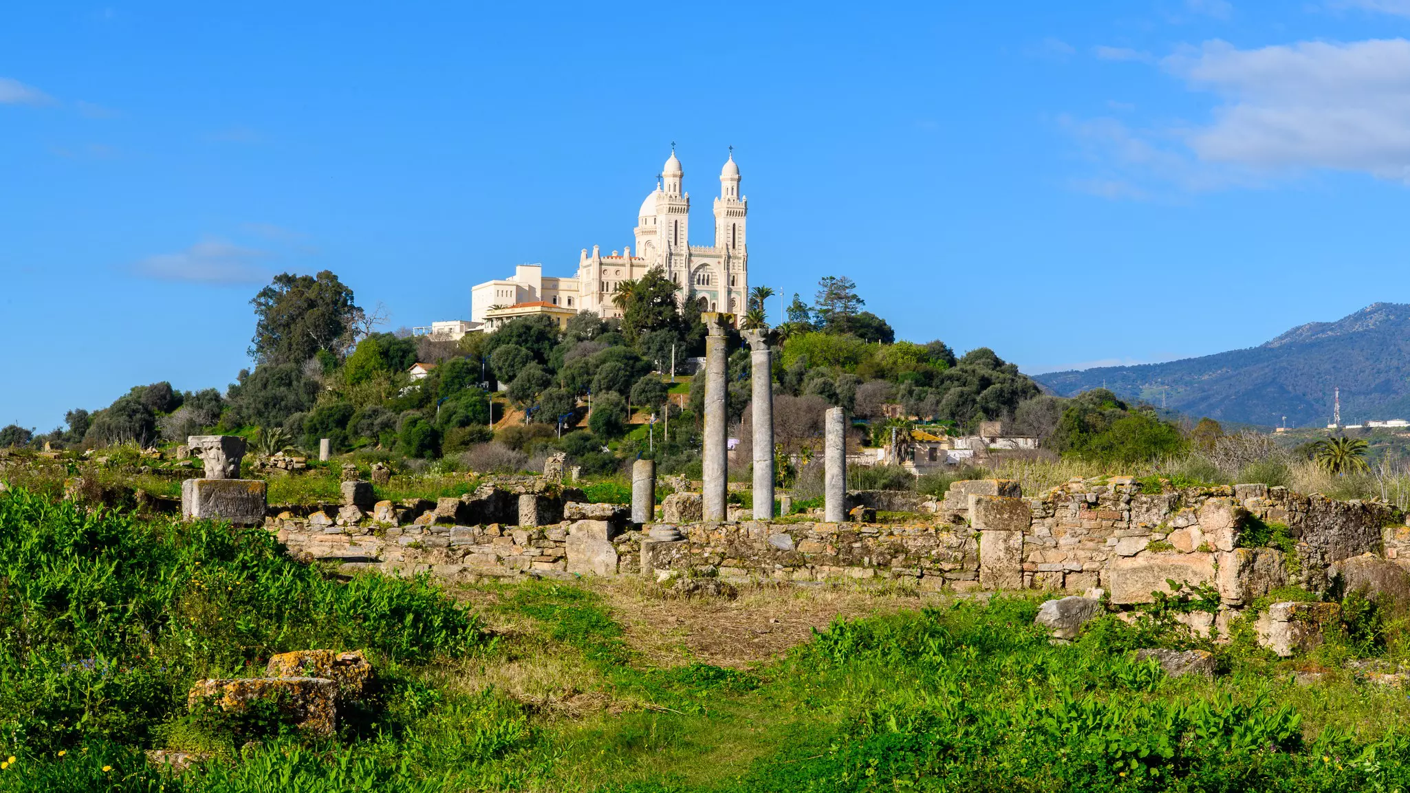 A hilltop basilica stands above a field of ruined Roman columns.