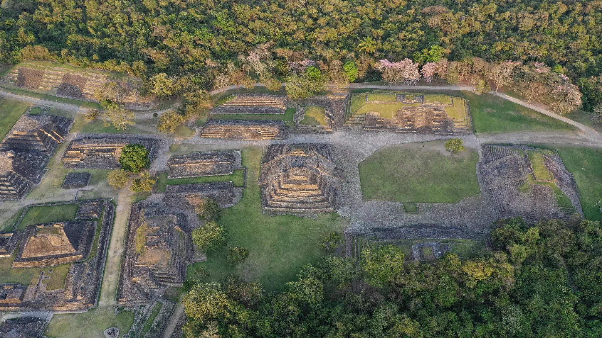 Aerial view of an ancient town with pyramids and other structures surrounded by lush forest.