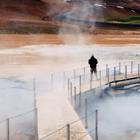 One person on a walkway through a geothermal area on an overcast day.
