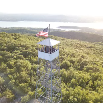 A woman in a tower with an American flag, looking out over the Hudson River, greenery and mountains