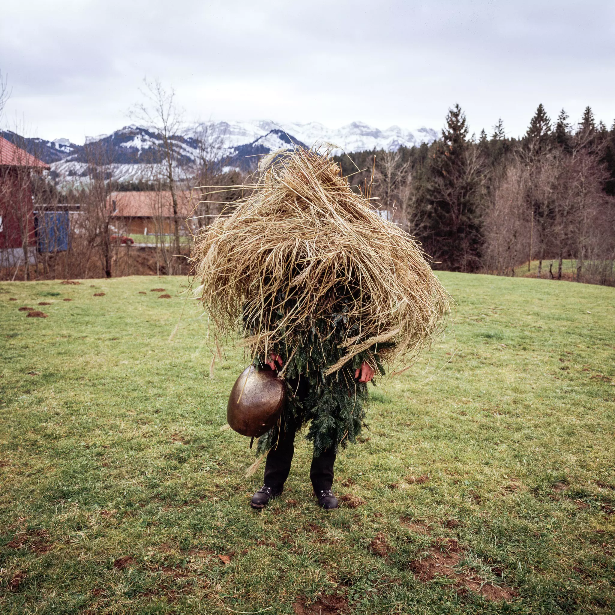 A person wearing a costume made of dried grass and evergreens stands in grass.