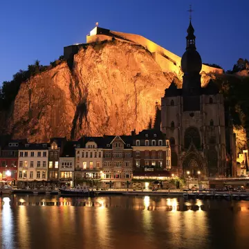 Historic downtown in Dinant, Namur, Wallonia, Belgium lit up at night with light reflecting off the water