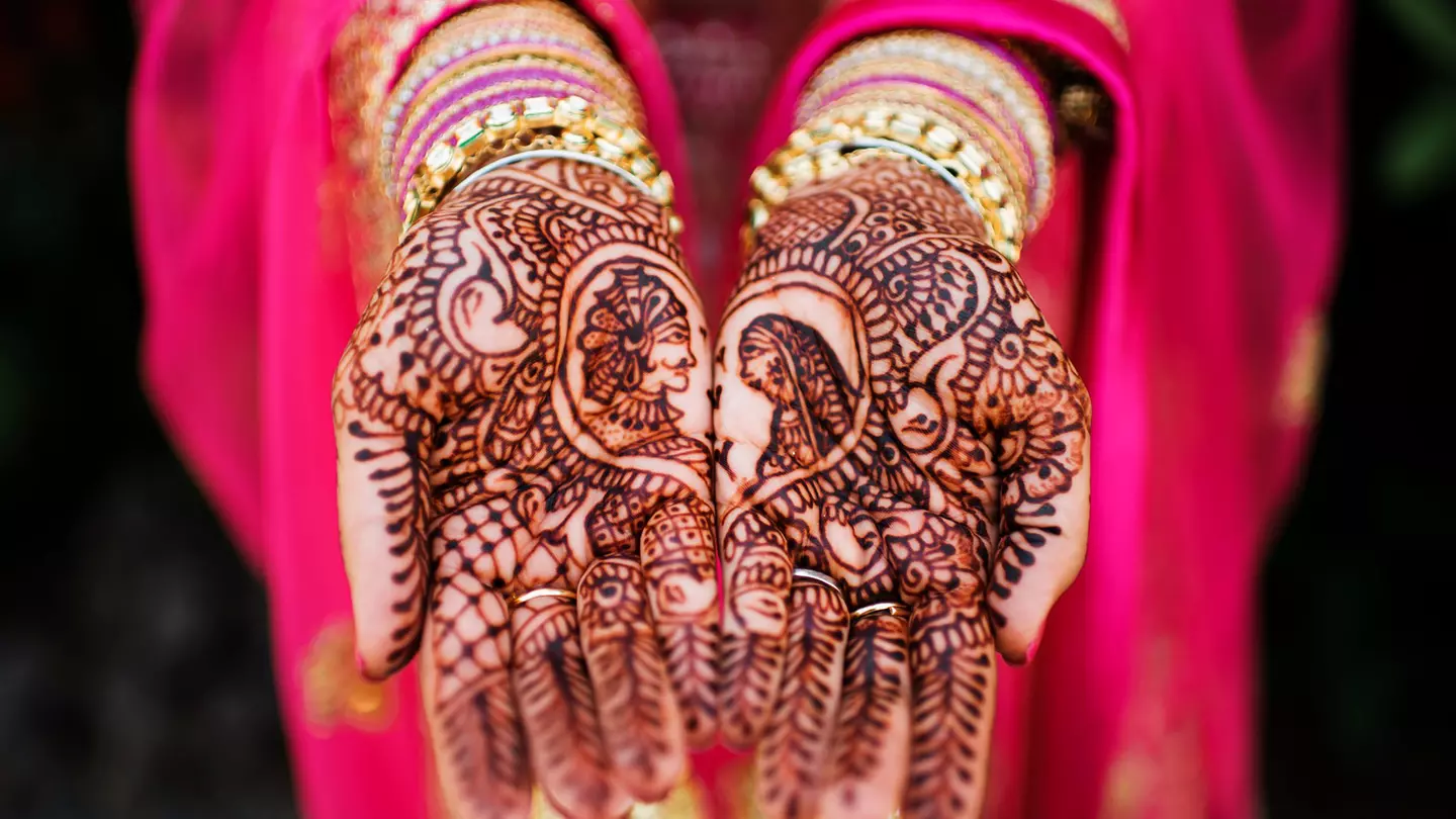 A bride in a bright pink sari shows off her henna designs on her hands