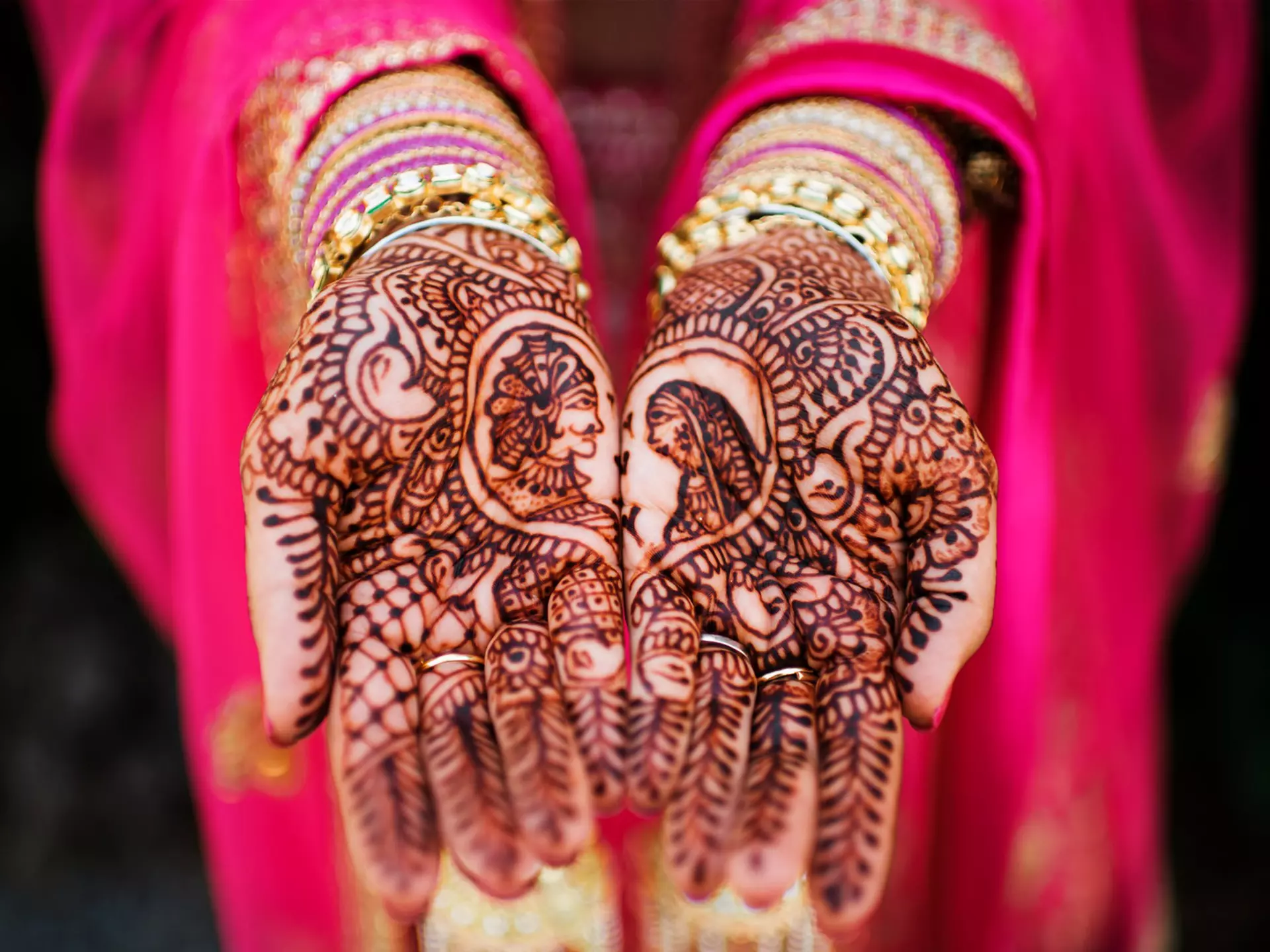 A bride in a bright pink sari shows off her henna designs on her hands