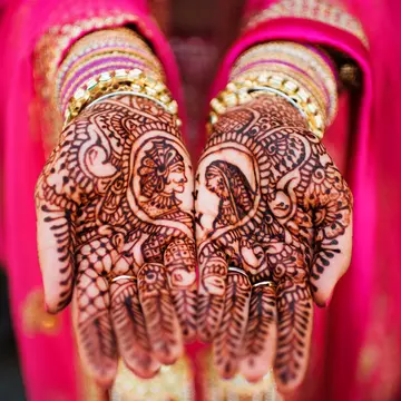 A bride in a bright pink sari shows off her henna designs on her hands