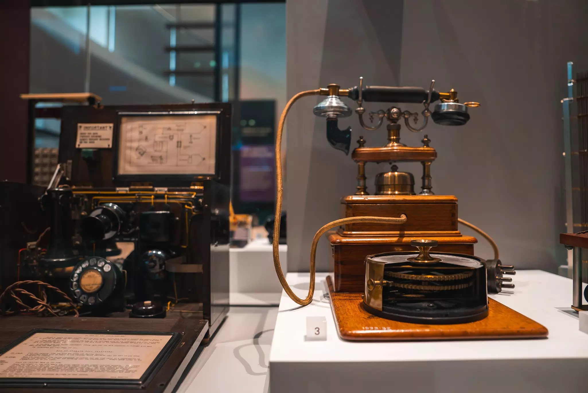 A vintage telephone with a wooden base, brass accents, and rotary dial is showcased in a museum