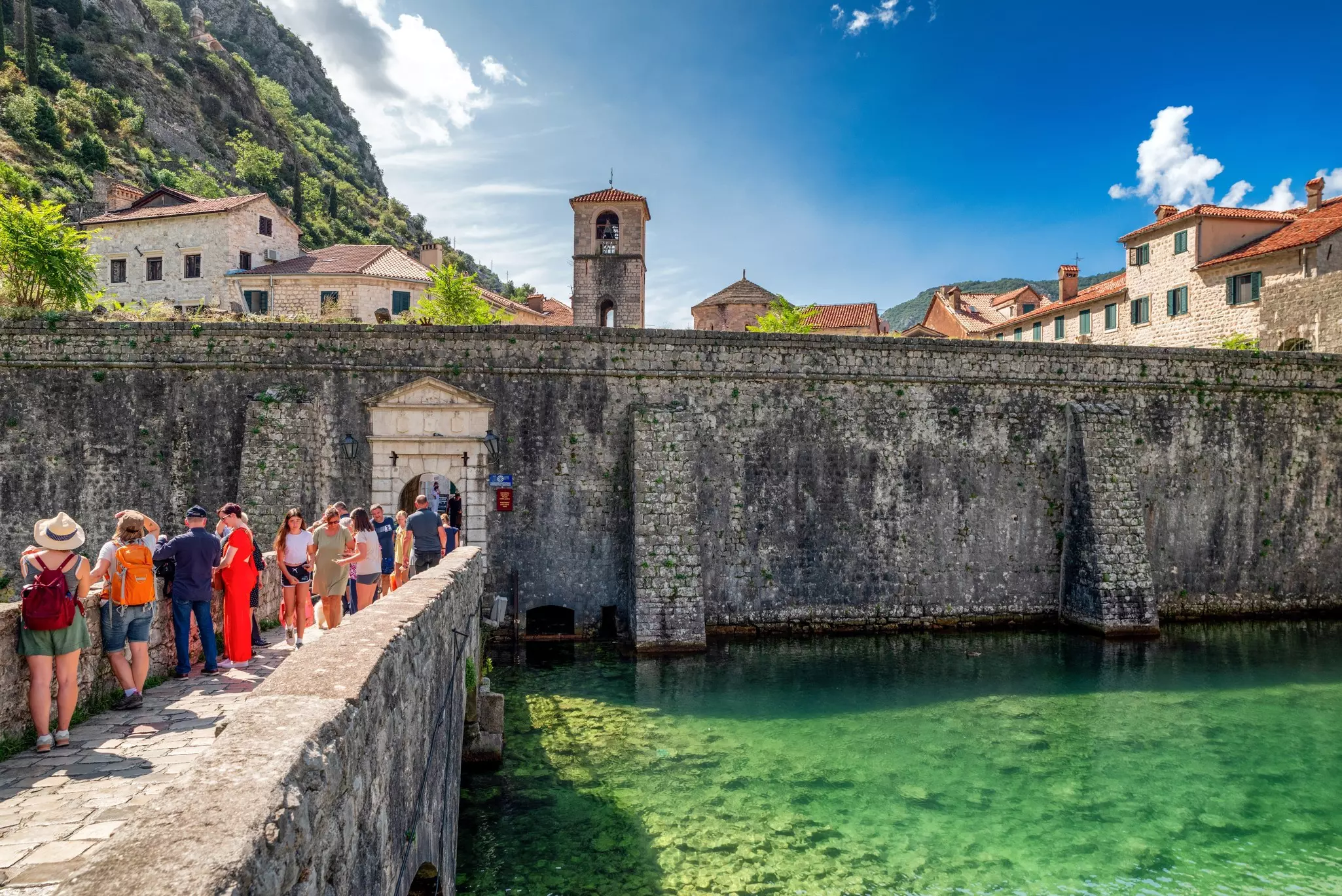 Tourists at the gate and walls of Old town of Kotor in Montenegro with clear sea, and bright sky above