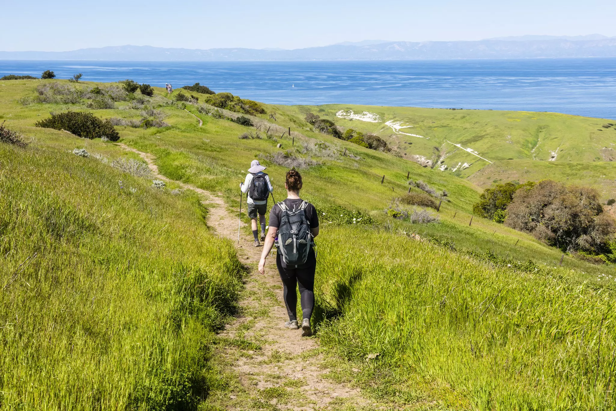 Two people following a hiking trail downhill towards the sea