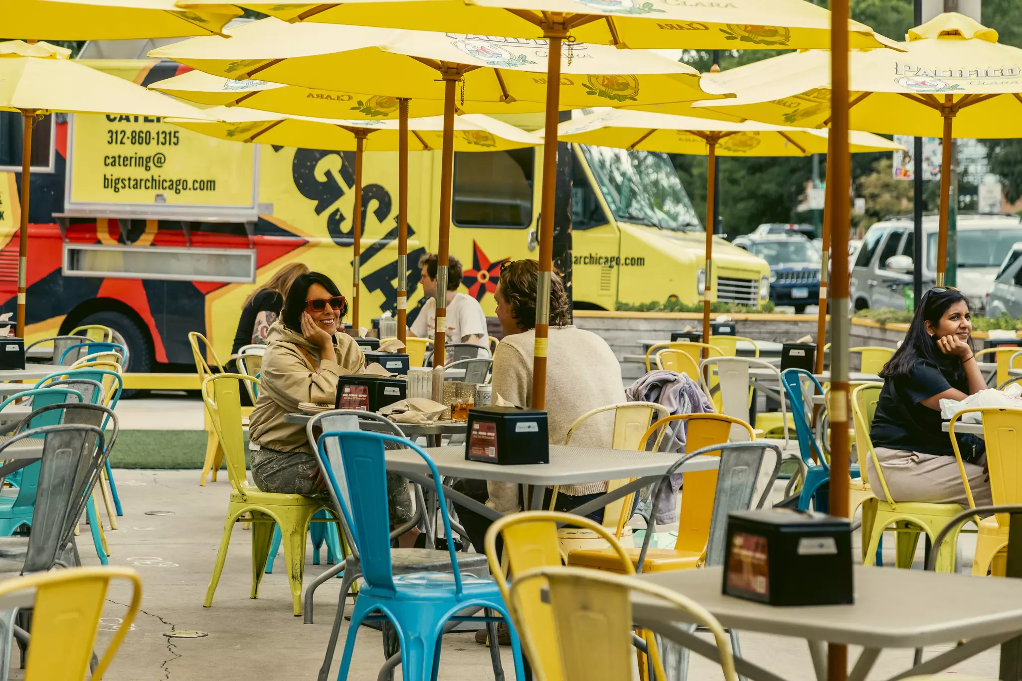 People sit at outdoor tables under yellow umbrellas.