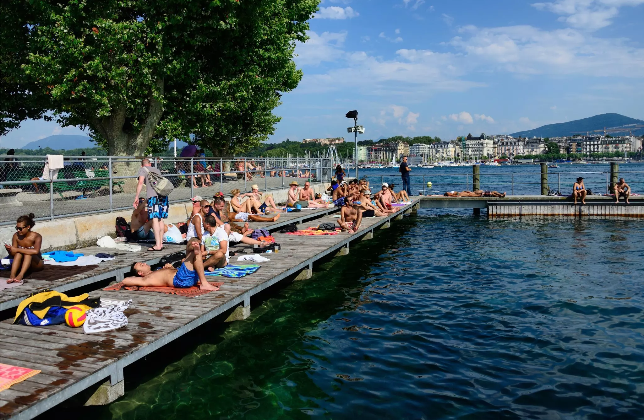 People lie in the sun on a dock over a lake in a city.