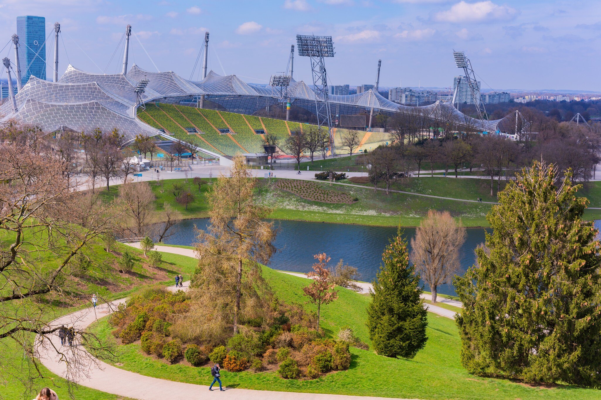 A scenic view of Olympiapark in Munich with lush green lawns and the distinctive Olympic Stadium in the background.