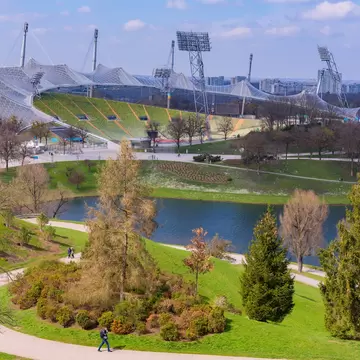A scenic view of Olympiapark in Munich with lush green lawns and the distinctive Olympic Stadium in the background.