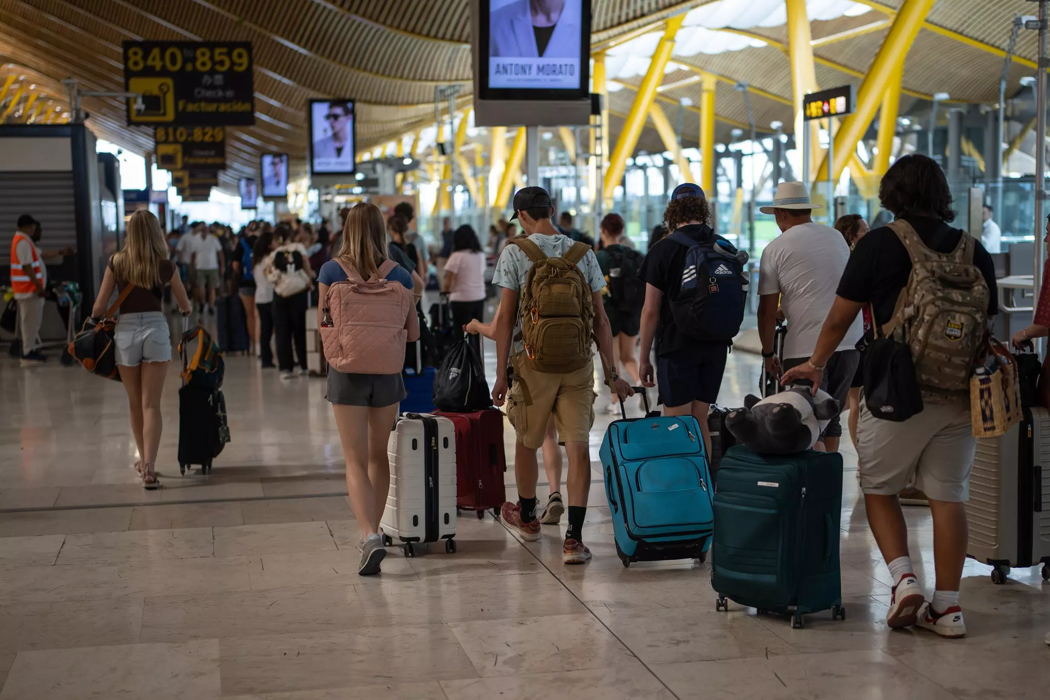 People with suitcases walk through a busy departure gate at an airport.