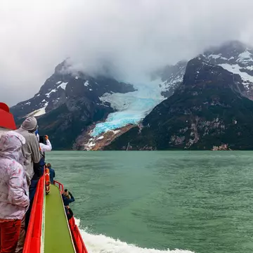 Tourists view a glacier from the deck of a red and white ship