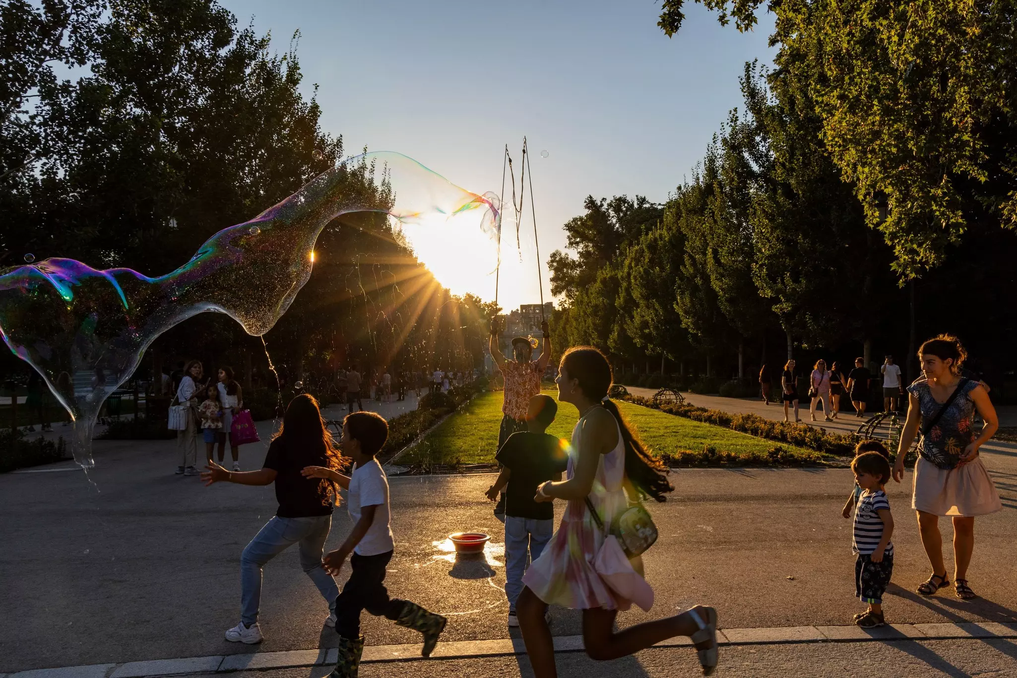 Children at sunset chase the soap bubbles of a street artist in a park in Madrid
