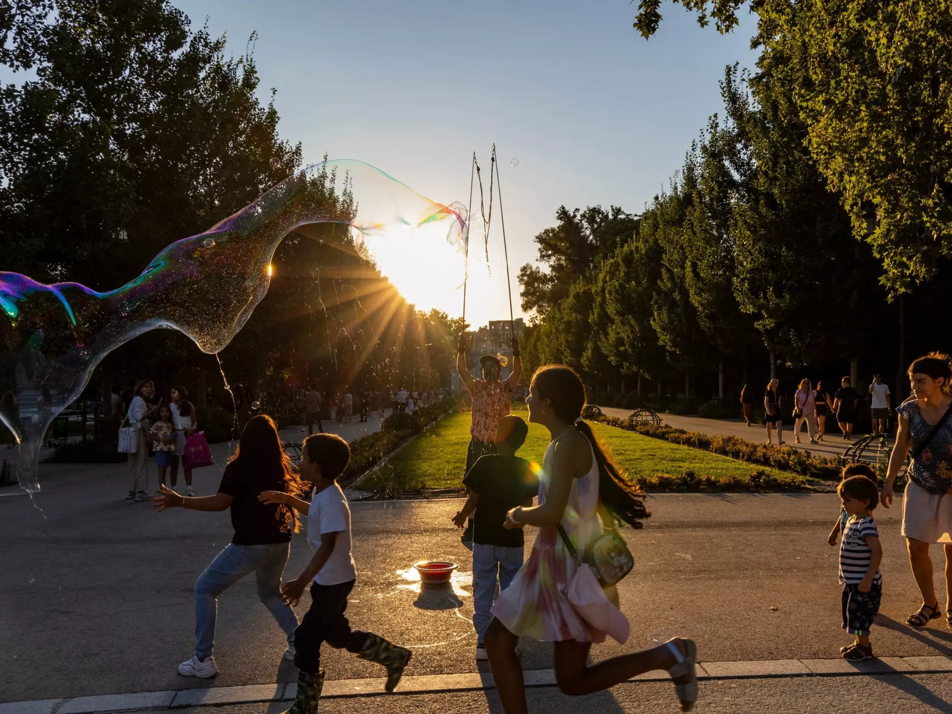 Children at sunset chase the soap bubbles of a street artist in a park in Madrid