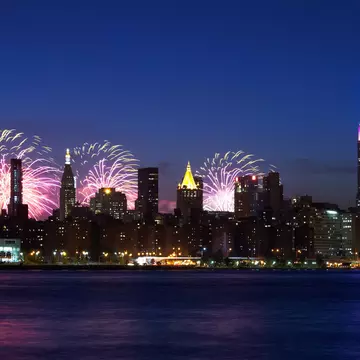 New York City skyline with the Empire State Building -- topped in red, white and blue -- at night with fireworks bursting behind them.