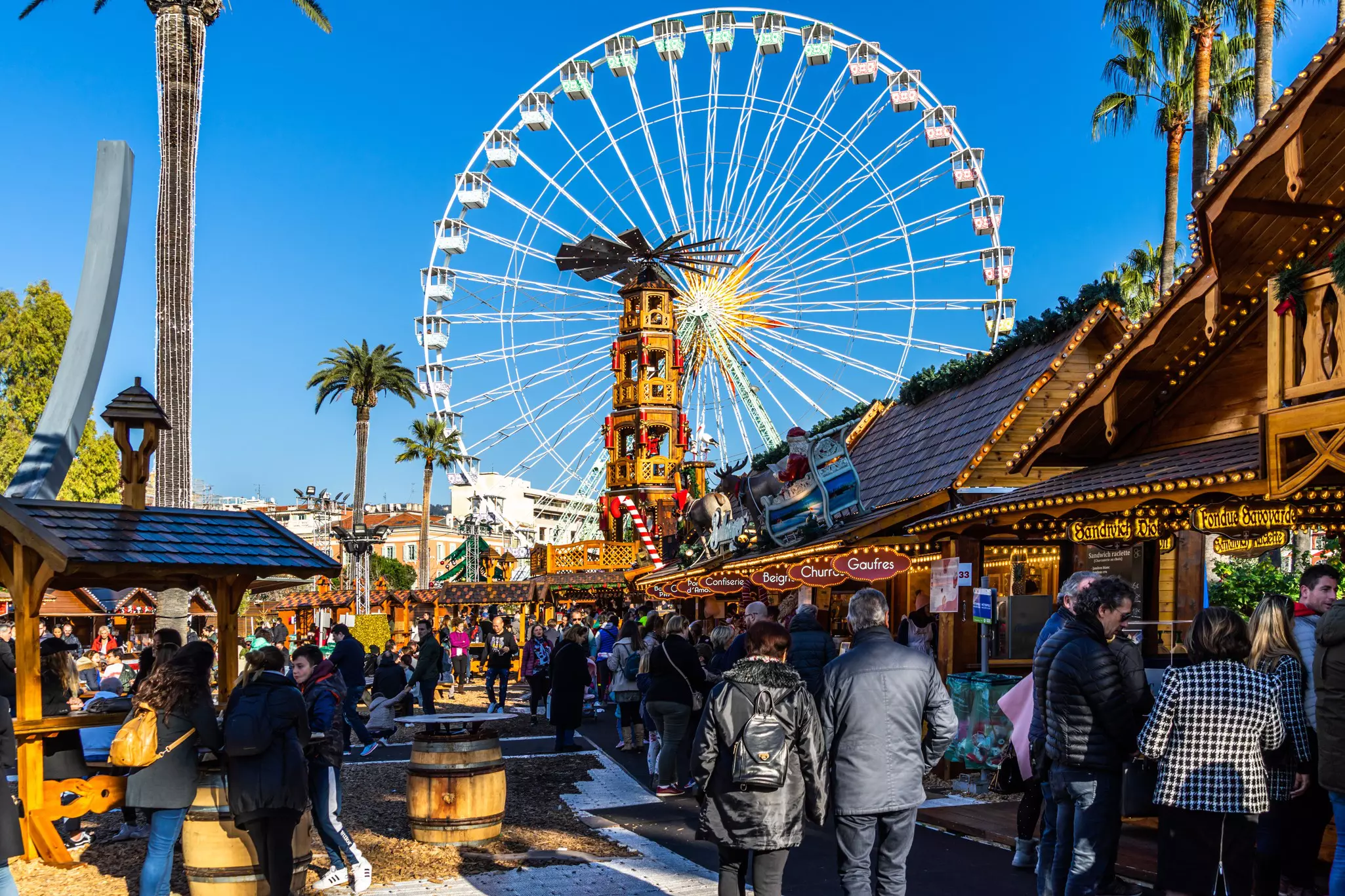 People shopping between the stalls of Nice Christmas market under the Ferris wheel