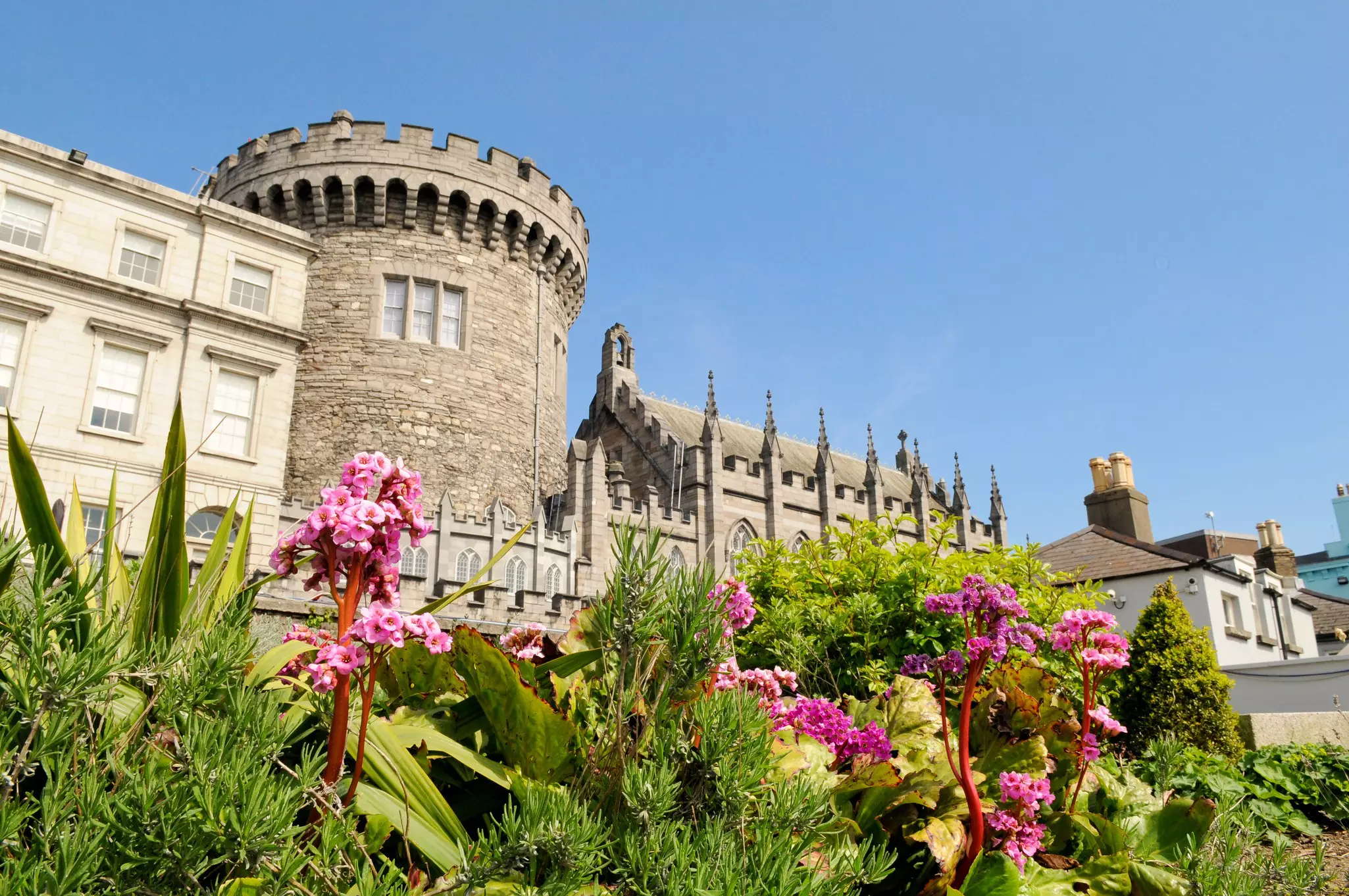 Stone castle with pink flowers and greenery in the foreground.