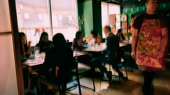 Blurred diners eat at tables against a window at a New York City restaurant.