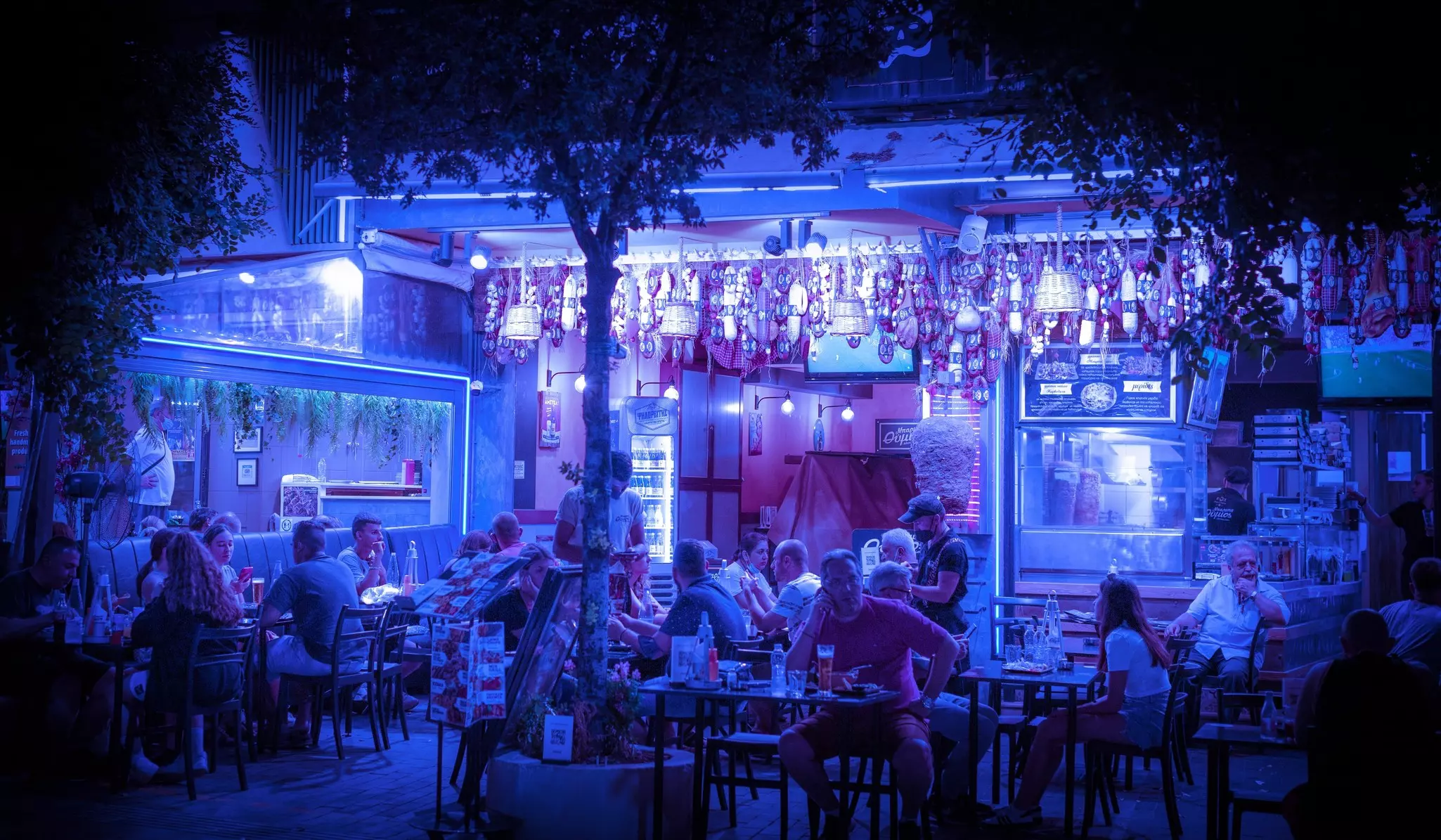 People sit at tables on an outdoor terrace at night, lit by evocative purple lights, Iraklio, Crete