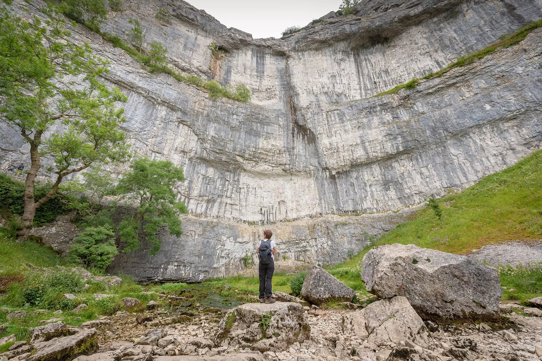 A hiker looks up at Malham Cove, Yorkshire Dales National Park, Yorkshire, England.