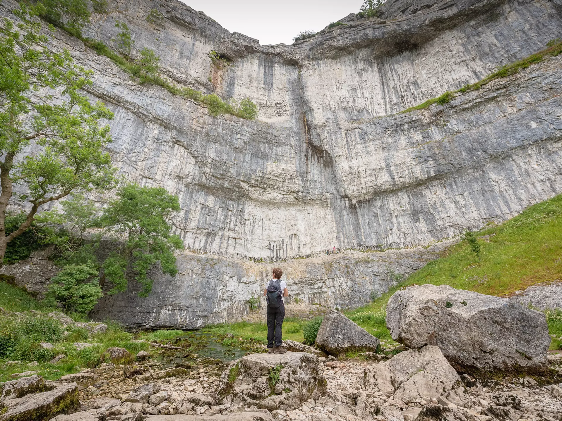 A hiker looks up at Malham Cove, Yorkshire Dales National Park, Yorkshire, England.