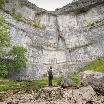 A hiker looks up at Malham Cove, Yorkshire Dales National Park, Yorkshire, England.
