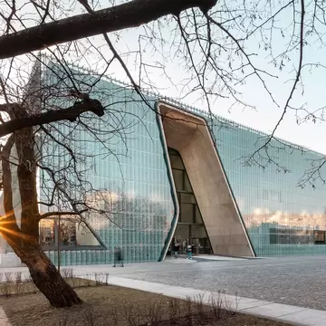Sunset light through bare branches beside a glass museum with a curved entrance cut.
