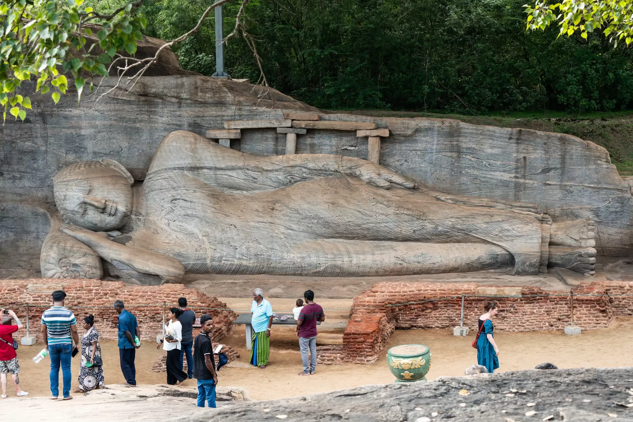People standing in front of a huge stone sculpture of a reclining Buddha