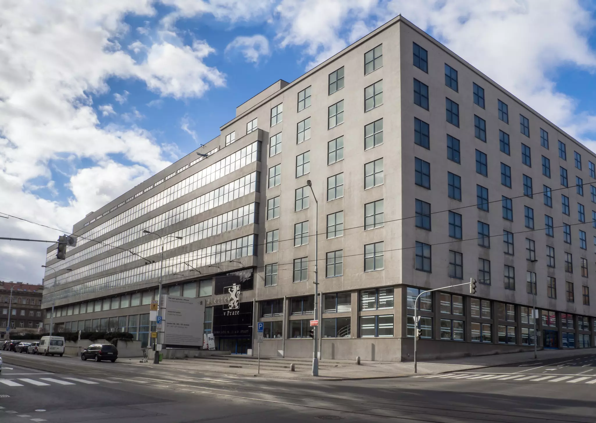 A large grey rectangular building at the corner of two streets in a city.