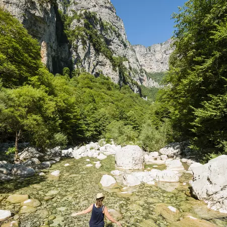Woman wading in clear fresh water of Voidomatis River in Vikos Gorge.