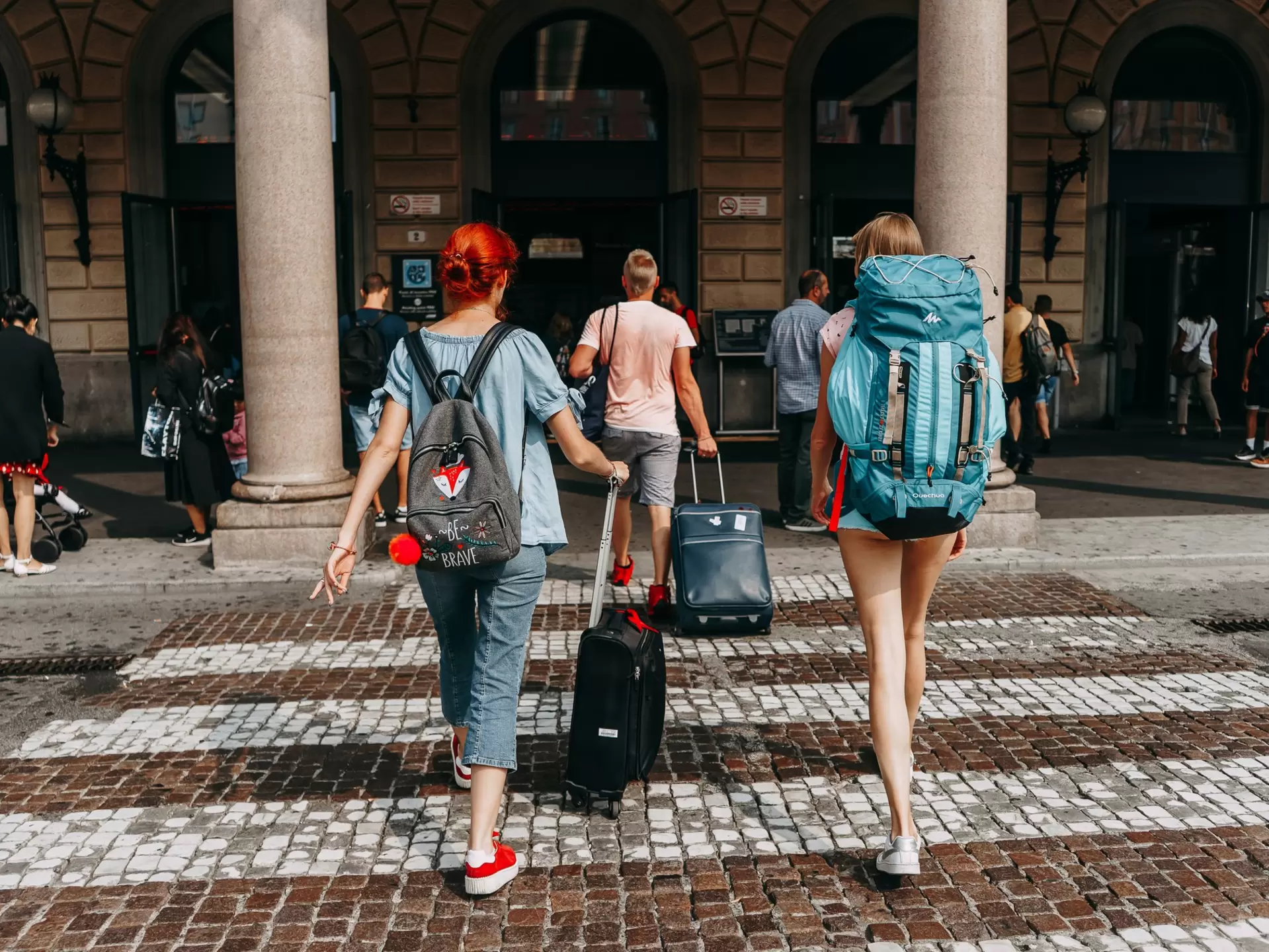 Tourists crossing the road at a pedestrian crossing in Italy with backpacks and suitcases 