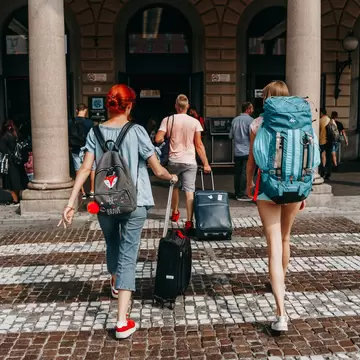 Tourists crossing the road at a pedestrian crossing in Italy with backpacks and suitcases 