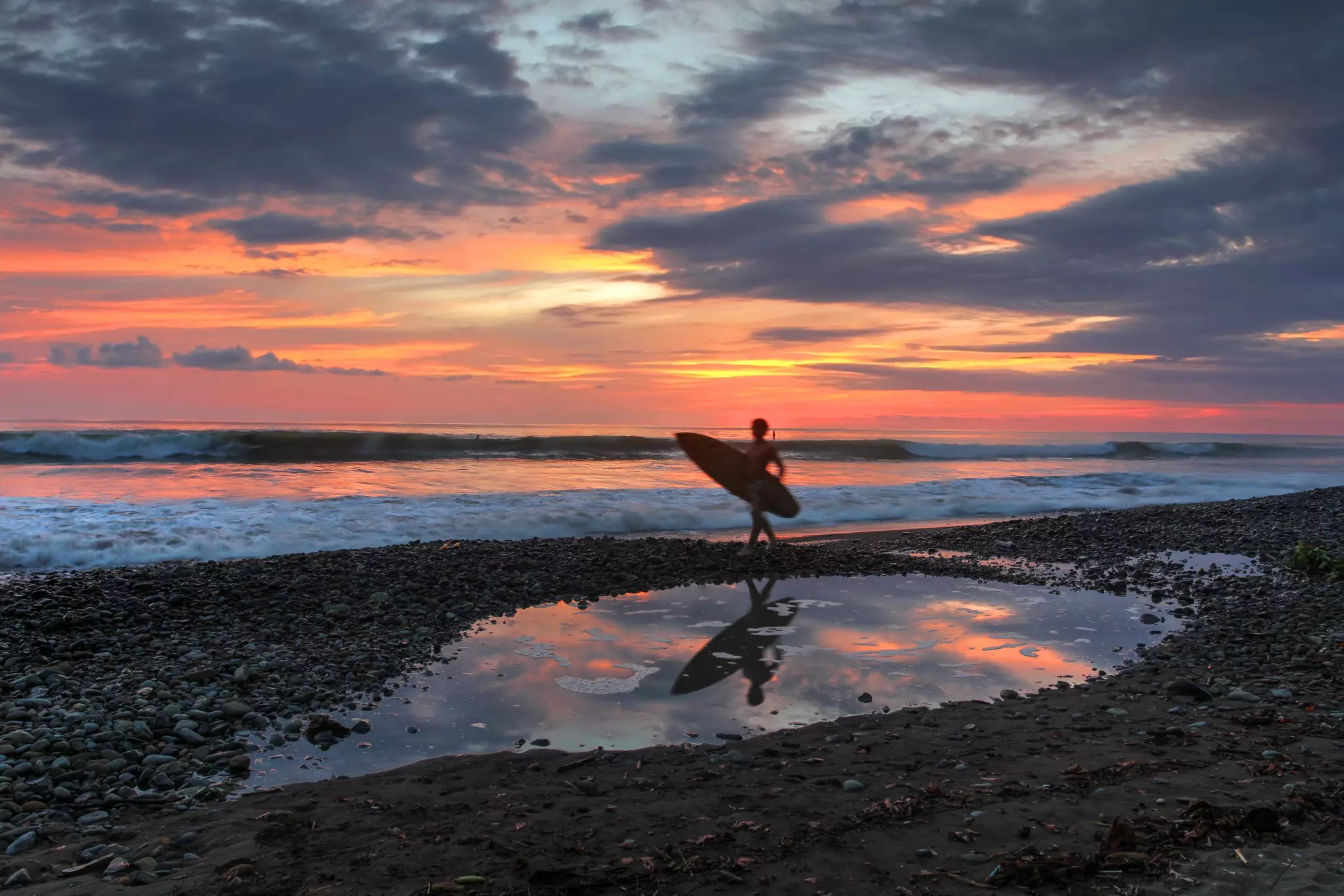 A surfer's destination, Playa Dominical in Costa Rica is a rocky beach settled mostly by foreign surfers. Sunset scene with surfers, waves and the setting sun reflecting in a tide pool. 