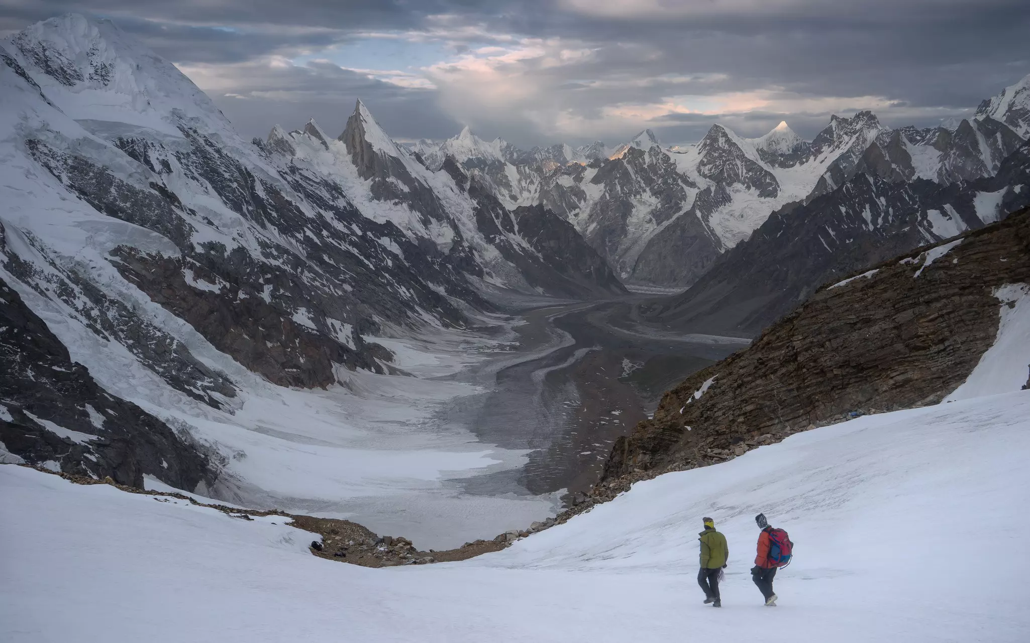 Two hikers make their way downwards into a mountain pass in very cold snowy conditions