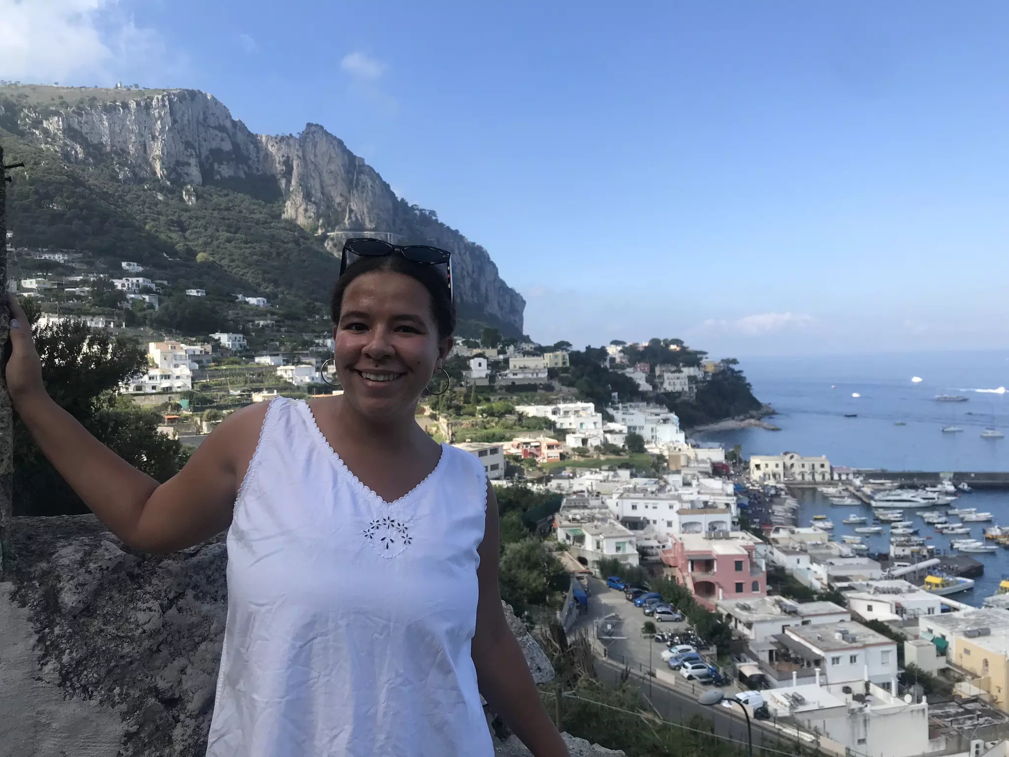 A woman standing on a cliff above a town and ocean on a sunny day.