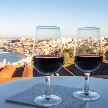 Two glasses of fortified wine on a table with a view over a riverside city.