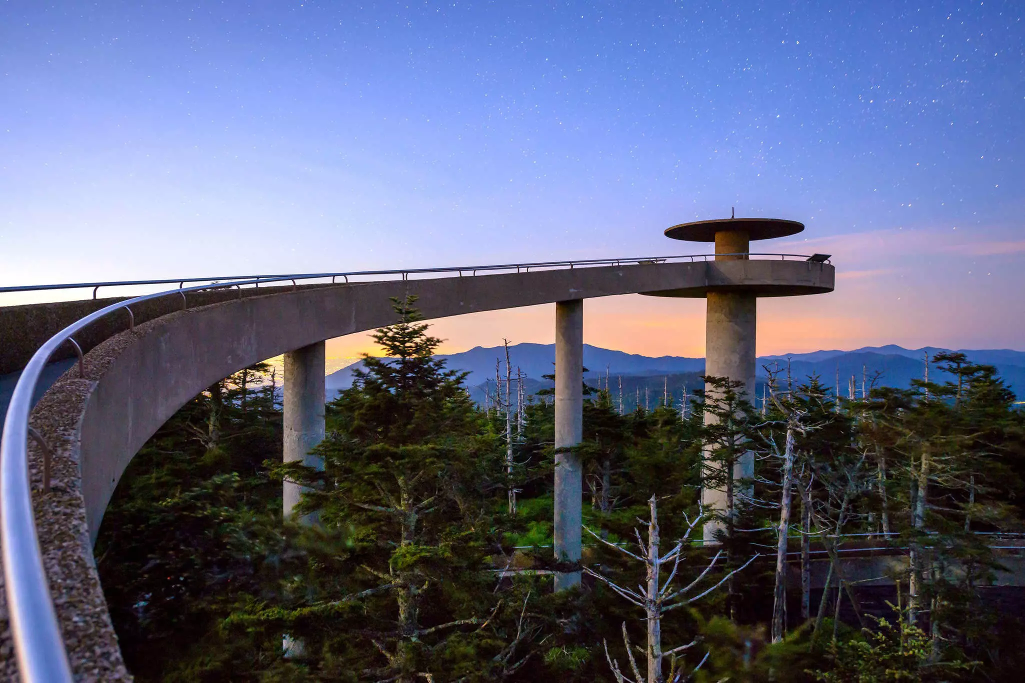 A curving, elevated walkway leading to a circular mountaintop observatory at sunset in the Great Smoky Mountains