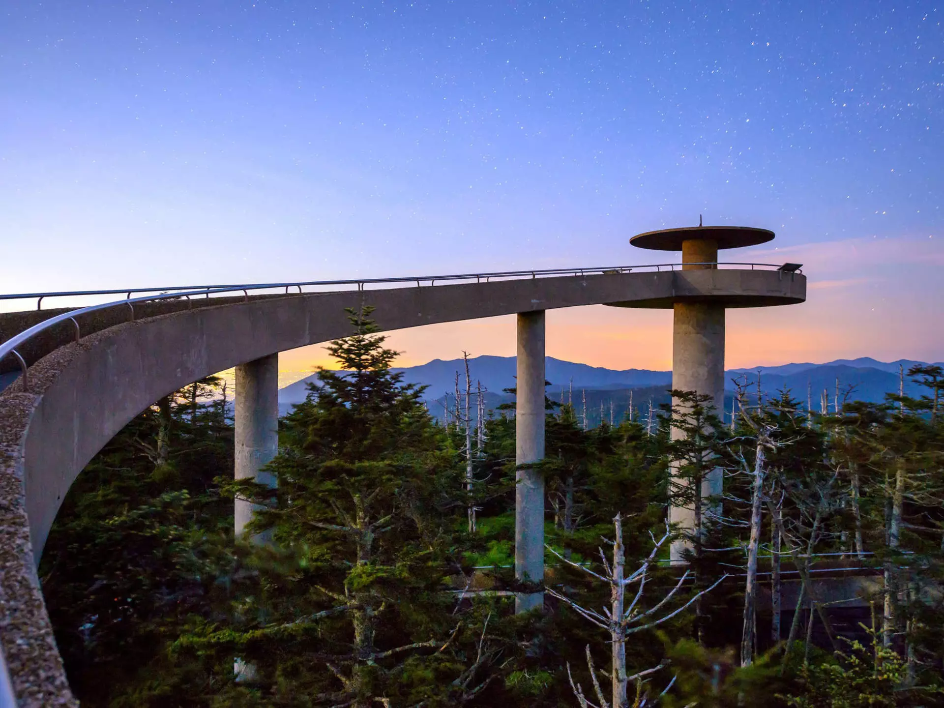 A curving, elevated walkway leading to a circular mountaintop observatory at sunset in the Great Smoky Mountains