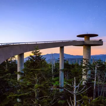 A curving, elevated walkway leading to a circular mountaintop observatory at sunset in the Great Smoky Mountains