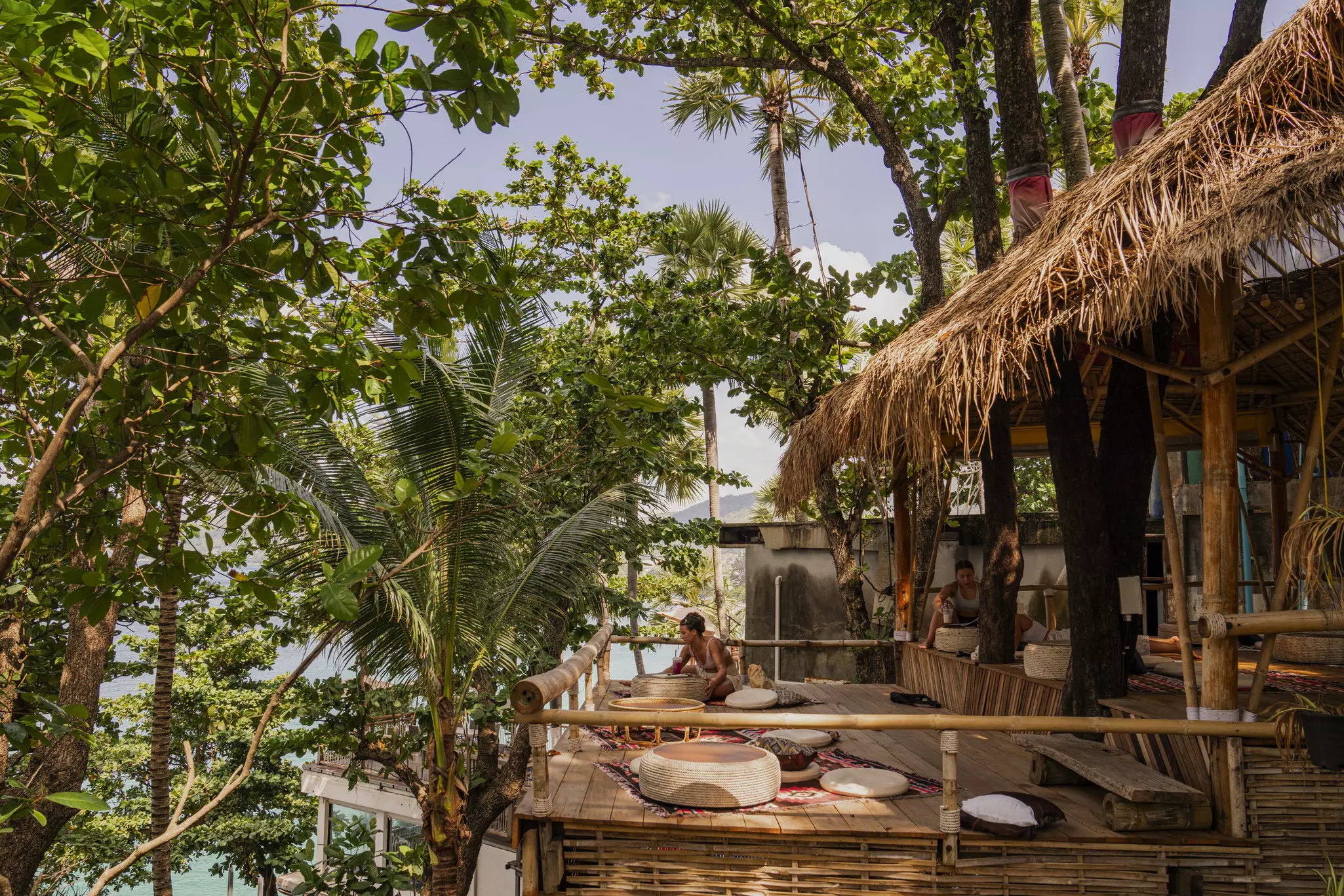 A woman sits at a wooden terrace cafe overlooking a beach