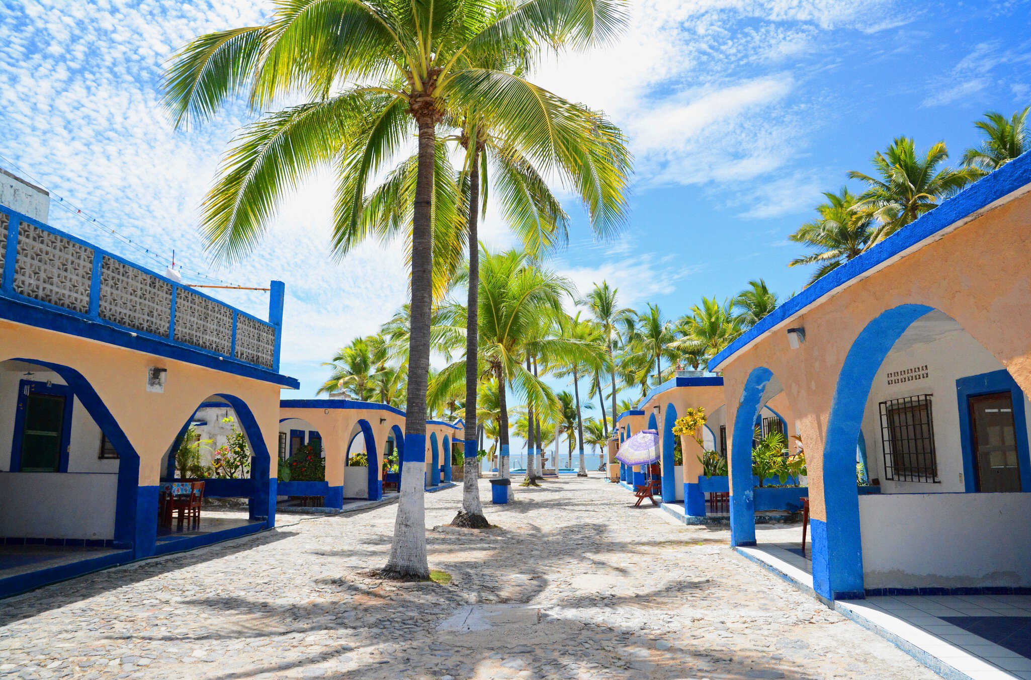 Melaque, Mexico. March 2015. Traditional Mexican single unit bungalows with palm trees and stone embedded  road.