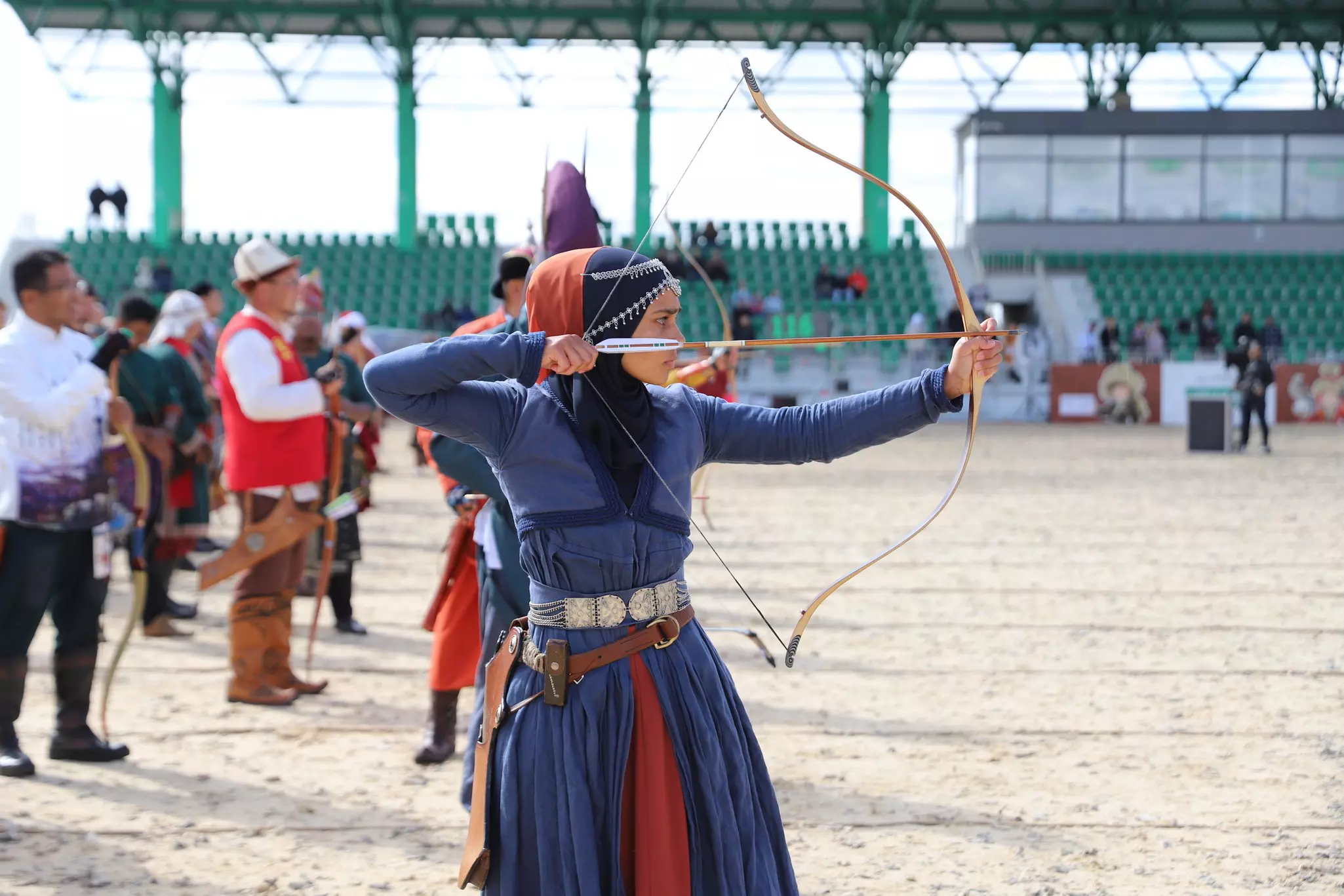 A woman in a headscarf uses a bow and arrow at an archery competition.