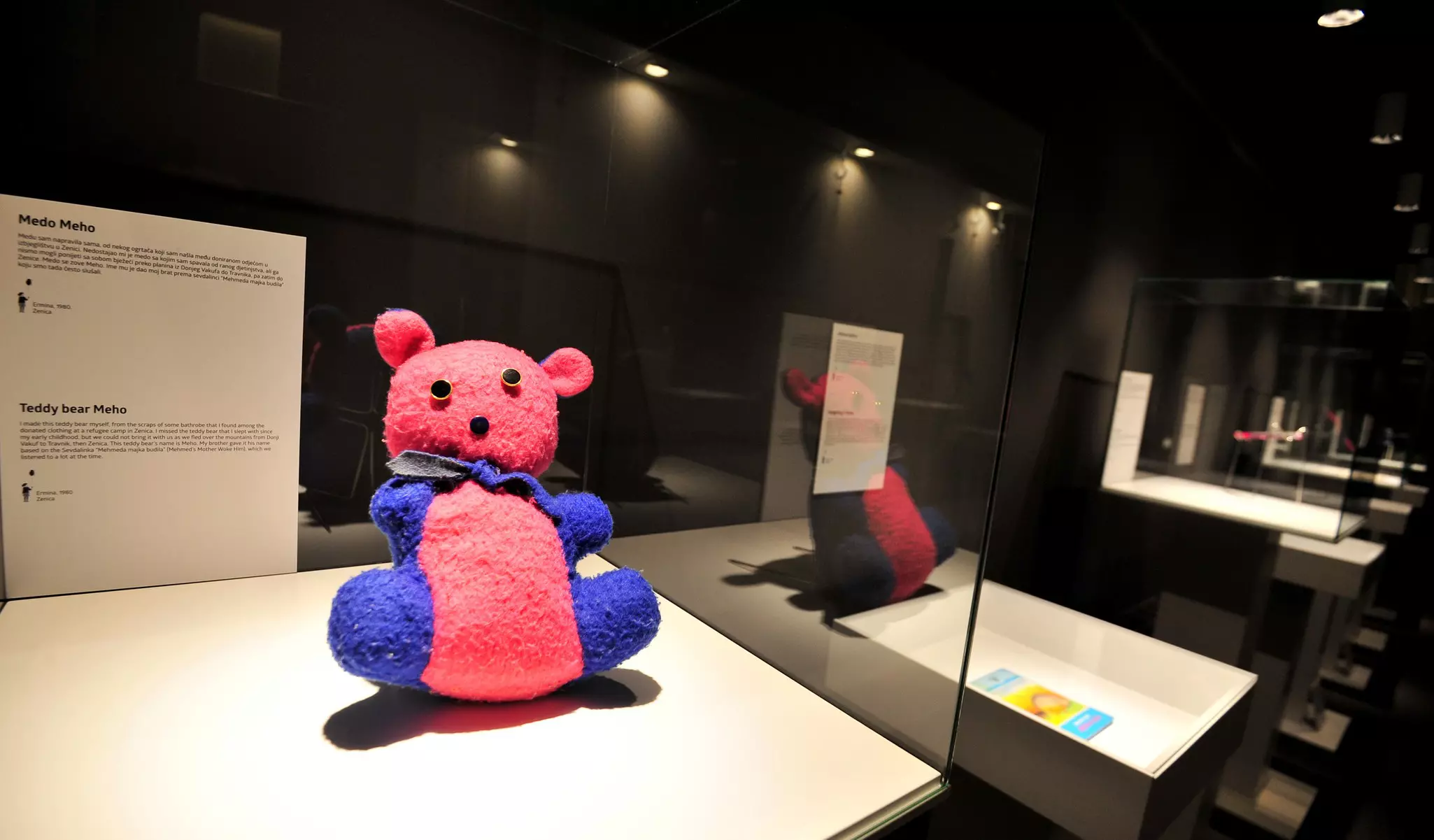 A homemade teddy bear displayed in a glass case at a museum.